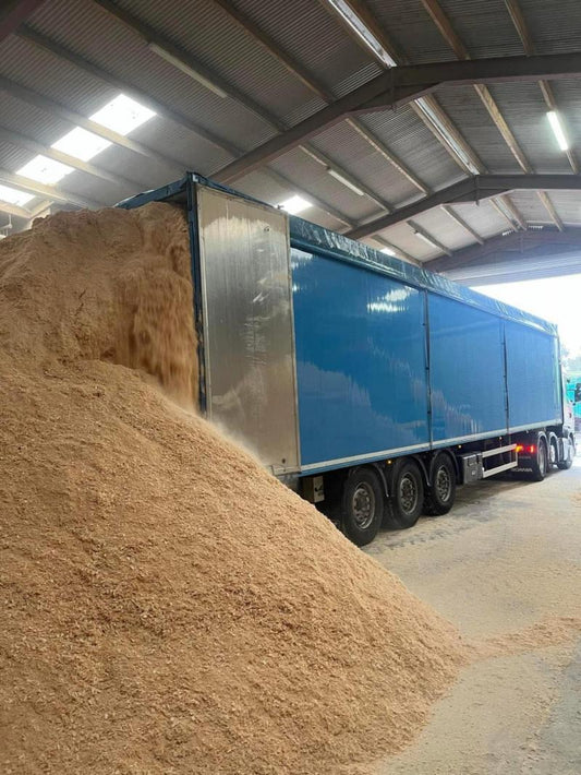 Blue truck parked next to a large pile of sawdust inside a building.