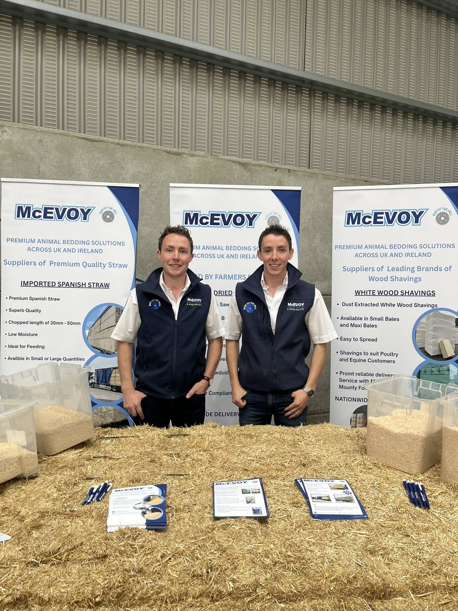 Two individuals standing in front of McEvoy banners with straw on the ground.